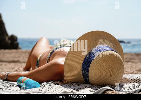 donna anziana irriconoscibile che prende il sole sdraiata sulla spiaggia con protezione solare nelle vacanze estive Foto Stock