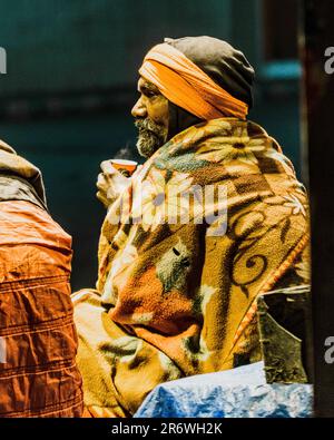 Un uomo avvolto in una coperta calda beve una bevanda calda in un ambiente esterno. Foto Stock