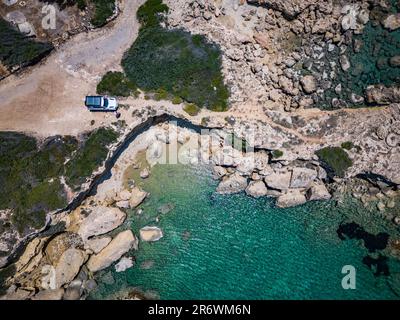 Vista aerea di un bianco off-roader in un viaggio su strada sulla costa della Grecia con turchese, acqua limpida e rocce Foto Stock