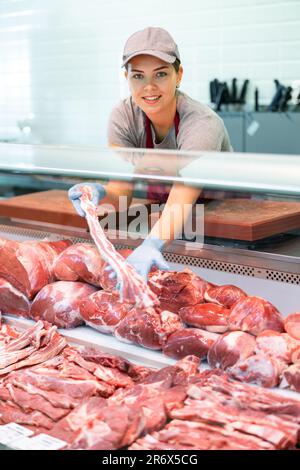 Il venditore giovane positivo in grembiule e guanti usa e getta mostra filetto di carne Foto Stock