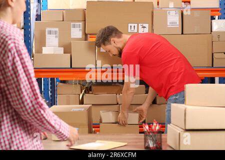 Donna e lavoratore che prendono il pacco dal rack all'ufficio postale Foto Stock