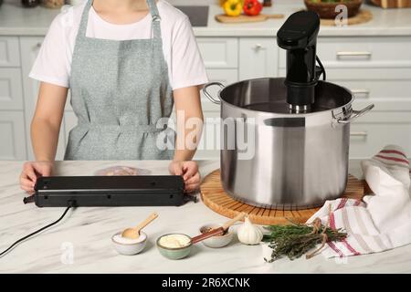 Donna che usa il sigillante per il confezionamento sottovuoto in cucina, closeup. Cucina sous vide Foto Stock