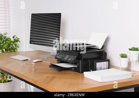 Stampante moderna con carta vicino al computer su un tavolo di legno in ufficio Foto Stock