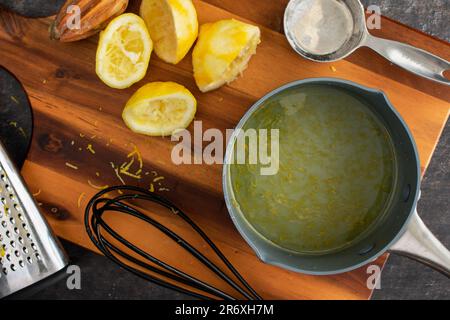 Sciroppo semplice al limone appena fatto in una pentola piccola: Sciroppo semplice al limone in una padella piccola circondata da ingredienti e utensili da cucina Foto Stock