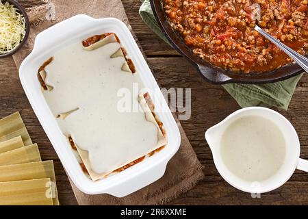 Preparazione di Lasagna in piastra rettangolare a casseruola. Beshamel o salsa bianca sulla parte superiore della salsa ragu o bolognese e del foglio di pasta di lasagne Foto Stock