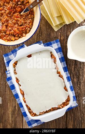 Preparazione di Lasagna in piastra rettangolare a casseruola. Beshamel o salsa bianca sulla parte superiore della salsa ragu o bolognese e del foglio di pasta di lasagne Foto Stock