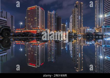Modalità notturna della città di Dubai. Grattacieli illuminati dello skyline con riflessi su una superficie d'acqua negli Emirati Arabi Uniti. auto parcheggiate davanti Foto Stock
