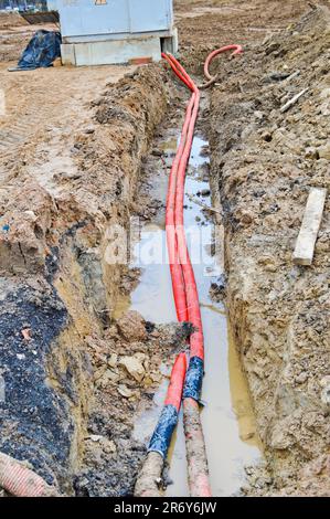 Grandi tubi corrugati in plastica rossa con fili per una sottostazione di trasformatori in un cantiere durante una riparazione in una nuova comunità sotterranea. Foto Stock