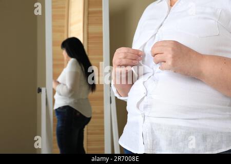 Donna sovrappeso cercando di buttare su camicia stretta a casa, primo piano Foto Stock