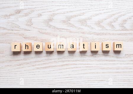 Parola Rheumatism fatto di cubetti su tavolo di legno bianco, vista dall'alto Foto Stock