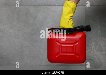 Uomo in guanto di gomma che tiene il barattolo rosso vicino alla parete grigia, primo piano. Spazio per il testo Foto Stock