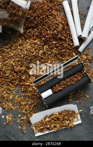 Composizione a giacitura piatta con rullo e tabacco su tavolo grigio scuro. Fare le sigarette arrotolate a mano Foto Stock