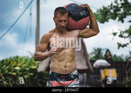 Uomo che si esercita con la palla medica, Canggu, Bali, Indonesia Foto Stock