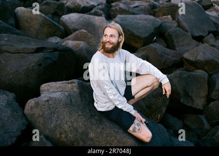 Uomo seduto sulle rocce, Canggu, Bali, Indonesia Foto Stock