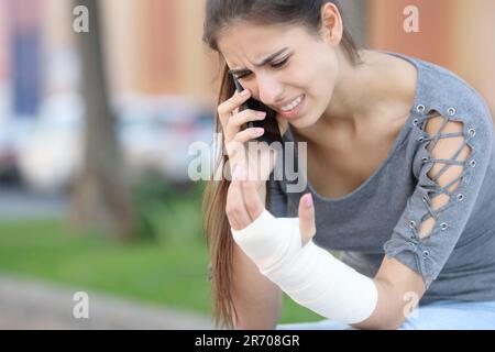 Donna convalescente con braccio bandito che chiama medico al telefono seduto in strada Foto Stock