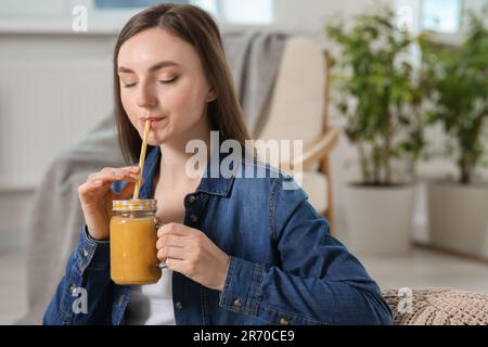 Bella giovane donna che beve frullato delizioso a casa Foto Stock