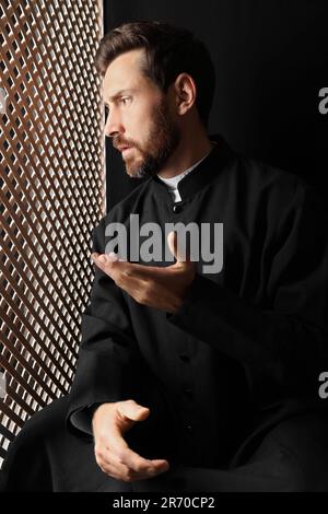 Sacerdote cattolico in cassock parlando con parishitoner in confessionale Foto Stock