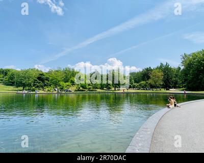 La vista del Beaver Lake Fountain Park con due donne sedute sulla riva. Foto Stock