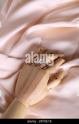 Gioielli eleganti. Mano manichino in legno con anello di lusso su tessuto rosa, vista dall'alto Foto Stock