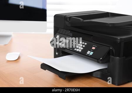 Stampante moderna con carta vicino al computer su un tavolo di legno in ufficio Foto Stock