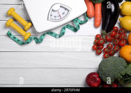 Bilance, metro a nastro, manubri, frutta e verdura fresca su tavola di legno bianco, giacitura piatta con spazio per il testo. Dieta a basso indice glicemico Foto Stock