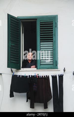 Donna a una finestra aperta, da un po 'di lavanderia asciugando su una clothesline in una città italiana Foto Stock