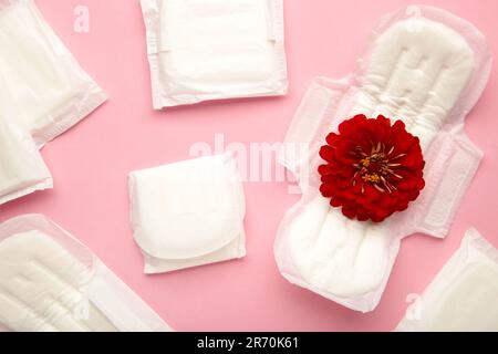 Pastiglie mestruali su sfondo rosa. Un fiore di rosa si trova su un tampone mestruale. Ciclo mestruale. Igiene e protezione. Vista dall'alto. Foto Stock