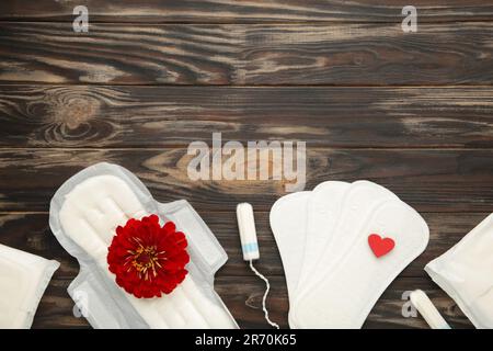 Tamponi e tamponi mestruali su sfondo marrone. Un fiore di rosa si trova su un tampone mestruale. Ciclo mestruale. Igiene e protezione. Vista dall'alto. Verticale Foto Stock