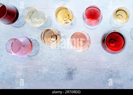Bicchieri da vino ad una degustazione. Vino rosa, rosso e bianco, bevande al tavolo in una cantina, scattate dall'alto. Un assortimento di vini di diversi colori Foto Stock