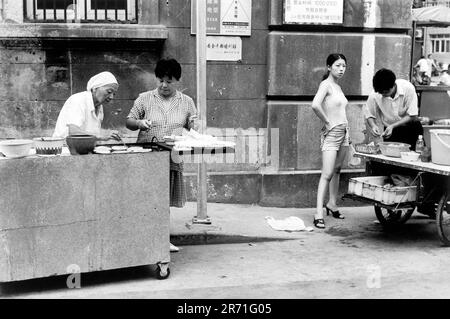 Shanghai Cina 2000. Fast Food è ovunque a Shanghai. Da bao zi per colazione: Gnocchi al vapore simili al pane ripieni di carne o verdure, uova da tè (cha ye dan) o riso glutinoso (zongzi) avvolto in foglie di banana o canne, c'è sempre qualcosa di gustoso a portata di mano. Qui il venditore di strada frigge pancake cinesi jian bing fatto da rape grattugiate, alcuni aromatizzati con cipolline. Di fronte sono disponibili gnocchi al vapore Nanxiang con aceto. 2000s OMERO SYKES Foto Stock