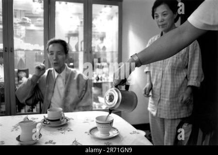 Shanghai Cina 2000. L'acclamato scultore in miniatura di Shanghai, Zhou Changxing, prende il caffè a casa di un amico. E 'considerato molto occidentalizzato per le persone della sua generazione di bere caffè, anche se dalla comparsa di Starbucks Coffee a Shanghai nel 1999 la bevanda ha iniziato ad attrarre i giovani come il bar è un buon posto per incontrare gli amici. Abiti comodi e sciolti sotto forma di pigiami sono spesso indossati all'interno di Shanghai, come negli anni '1920s, e non è raro indossare il pigiama fuori porta, soprattutto in estate. 2000s OMERO SYKES Foto Stock