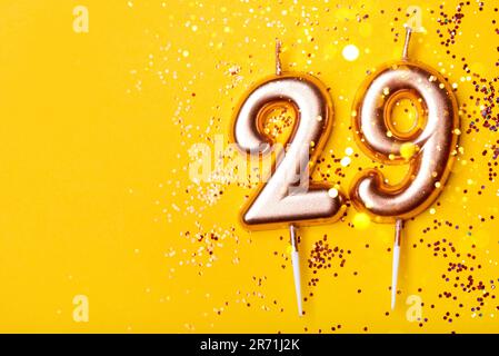 29 anni di celebrazione. Banner di saluto. Candele d'oro in forma di numero ventinove su fondo giallo con confetti. Foto Stock