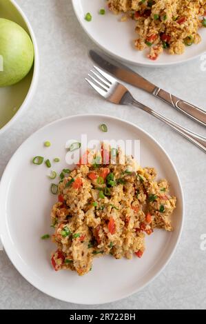 Riso bruno fritto con uova strapazzate, tonno e verdure su piatti su sfondo bianco Foto Stock