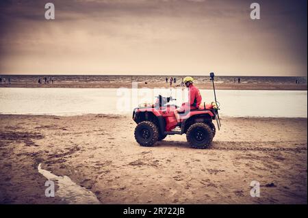 Bagnino in quad tenendo d'occhio gli utenti della spiaggia quando arriva la marea Foto Stock