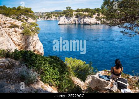 Giovane donna (non identificata; vista sul retro) ammirando la splendida vista di Calanque de Port-Miou con barche a vela ormeggio nel suo porto turistico. Francia. Foto Stock
