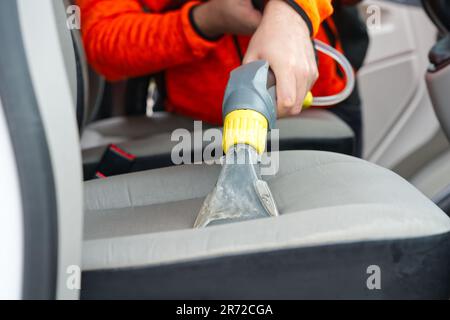 Sedile anteriore in tessuto per auto con aspirapolvere per uomo. uomo che pulisce la macchina da lavoro Foto Stock