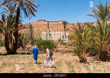 Terreno agricolo di fronte al pittoresco villaggio berbero di Tamenougalt nella valle del Draa, un turista che è guidato da un berbero al villaggio, Marocco Foto Stock