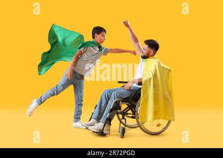 Il ragazzino e il padre in sedia a rotelle indossano cappe supereroi su sfondo giallo Foto Stock