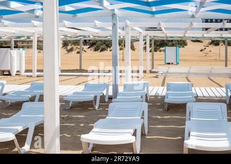 spiaggia di sabbia sulla costa del mare con lettini bianchi vuoti sotto un baldacchino di legno. Stazione balneare. Foto Stock