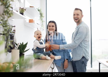 Ritratto di due bicchieri da tostare per adulti e bambini con succo di frutta e sorridente alla macchina fotografica. Simpatica famiglia caucasica gustando frullati freschi fatti in casa durante una dieta sana a casa. Foto Stock