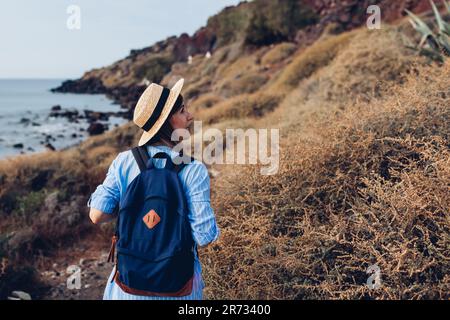 Donna viaggiatore con zaino a piedi sulla spiaggia da costa del mare godendo il paesaggio. Turismo, viaggi. Vacanze estive Foto Stock