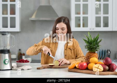 Donna che prepara gli ingredienti per gustosi frullati al tavolo in marmo bianco in cucina Foto Stock