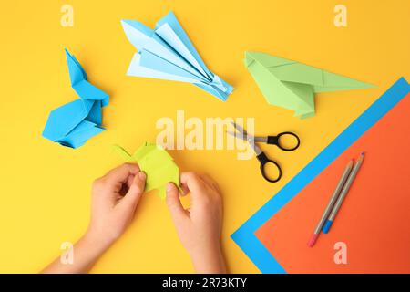 Origami art. Bambino che tiene figure di carta su sfondo giallo, primo piano e vista dall'alto Foto Stock