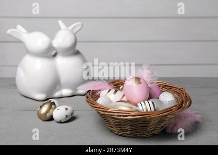 Cestino di vimini con uova di Pasqua decorate in modo festivo su un tavolo di legno grigio Foto Stock