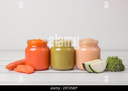 Vasetti di alimenti sani per bambini e verdure su un tavolo di legno bianco Foto Stock