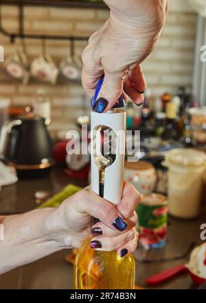 Donna apre una bottiglia di vino bianco con un cavatappi speciale Foto Stock