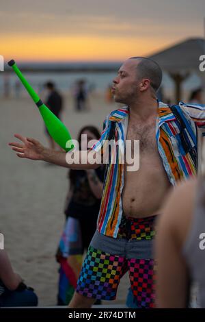 Giocoliere che cerca di destreggiarsi tra i club sulla spiaggia al tramonto Foto Stock