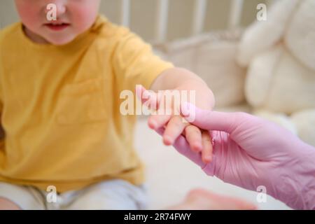 Il medico fa ginnastica e massaggio delle mani ad un bambino del toddler. Infermiera in uniforme facendo esercitazioni ortopediche del dito della mano al bambino. Bambino di circa due anni Foto Stock