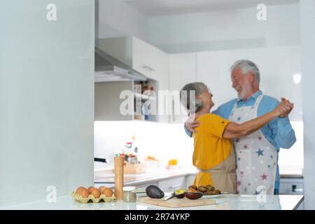 Una coppia di famiglie di mezza età che ballano a tutta lunghezza con musica da discoteca in cucina. Felice vecchio uomo e donna che si divertono, intrattenendo insieme al chiuso, coinvolto in divertente attività domestica. Foto Stock