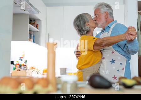 Una coppia di famiglie di mezza età che ballano a tutta lunghezza con musica da discoteca in cucina. Felice vecchio uomo e donna che si divertono, intrattenendo insieme al chiuso, coinvolto in divertente attività domestica. Foto Stock